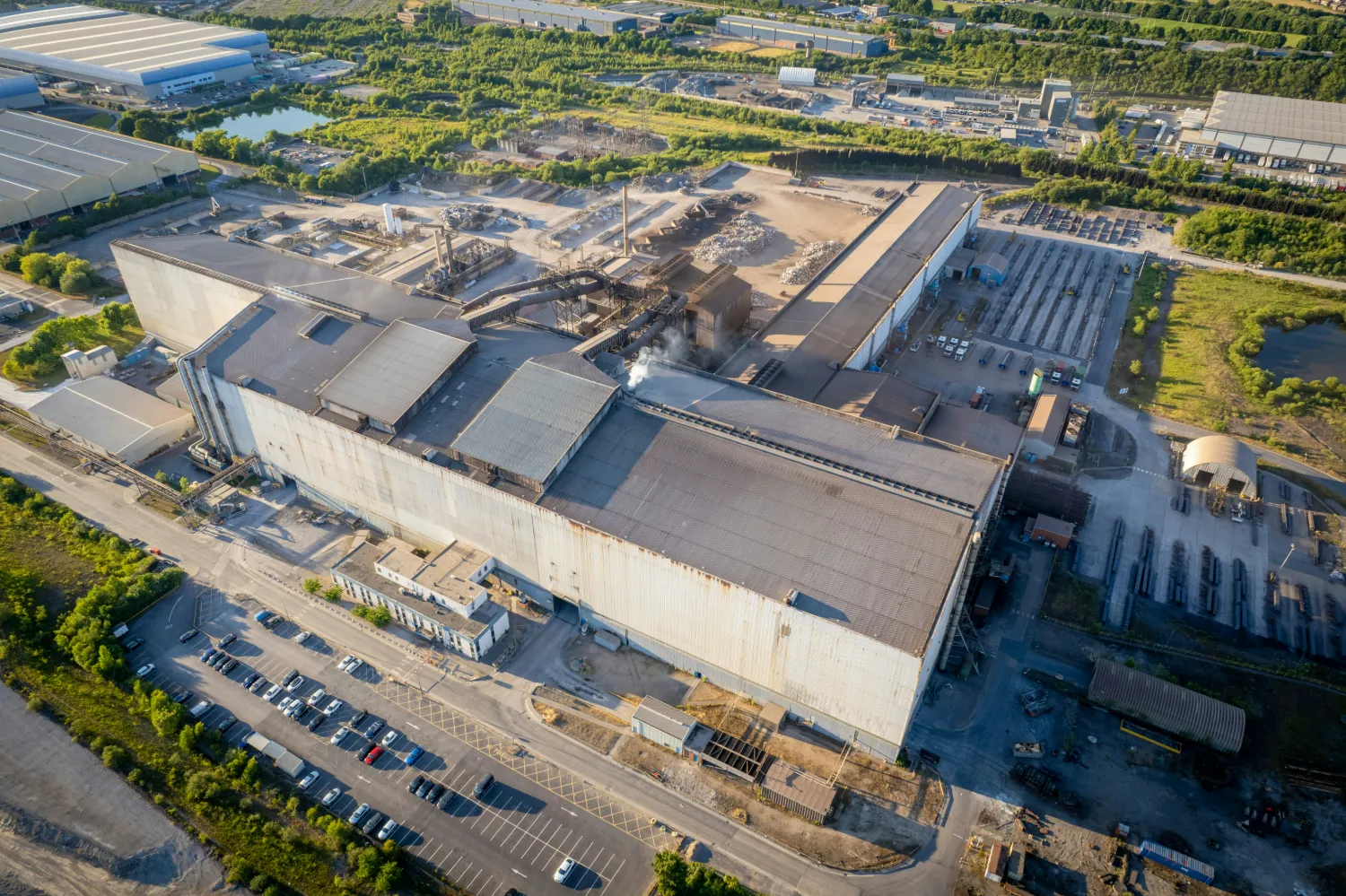 Widok z lotu ptaka na zakład produkcyjny z halami, placem składowym i parkingiem